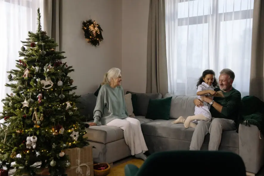 Noël chez les séniors Un couple de personnes âgées dans leur canapé avec leur petite fille en train d'ouvrir les cadeaux de Noël autour du sapin.