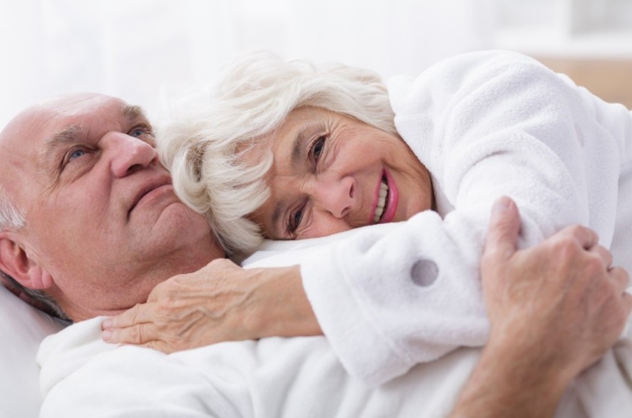 Le sexe durant la vieillesse 2 Un couple de séniors en robes de chambre blanches allongés l'un sur l'autre.
